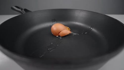 Rohes Ei fällt in die Pfanne und zerschlägt in Zeitlupe, fallendes Ei in 240 Bildern pro Sekunde, Kochen in der Küche