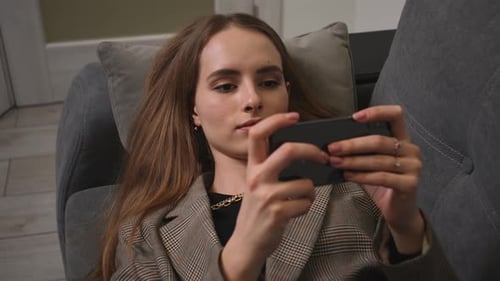Chica relajada que sostiene un teléfono inteligente usando aplicaciones móviles Juega juegos viendo Vídeo acostada en el sofá de casa