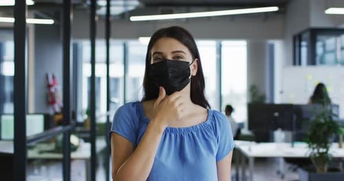 Portrait of caucasian businesswoman adjusting face mask standing in office and looking to camera