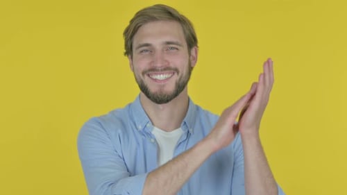 Junger Mann klatscht applaudierend auf gelbem Hintergrund