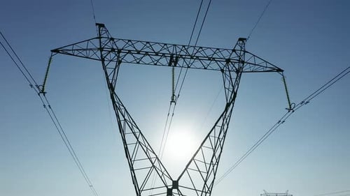 Transmission tower supporting an overhead high voltage power line silhouette at sunrise.