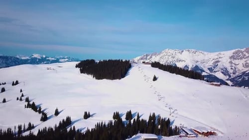 Ski resort in sunny weather. Snow on the ski slope of a wooded mountain. Many tourists near the ski