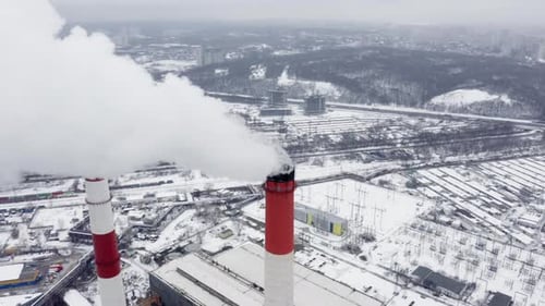 Aerial Observation of Snowy Industrial City with Two Huge Smoking Factory Pipes at the Foreground