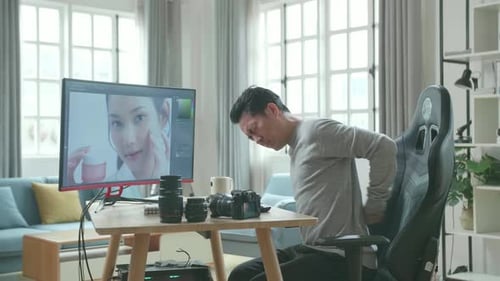 Man Editing Pictures at Desk Stretches Back