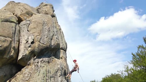 Strong Male Climber Descending Down Steep Wall of Rocky Mountain