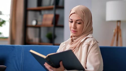 Mujer musulmana en hijab pañuelo en la cabeza leyendo libros religiosos vintage literatura afición en casa sofá