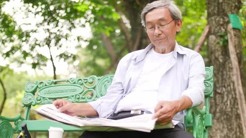 Asian senior man sitting in the park and reading a newspaper