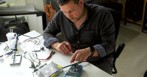 Man Testing Electronic Components at Desk Indoors
