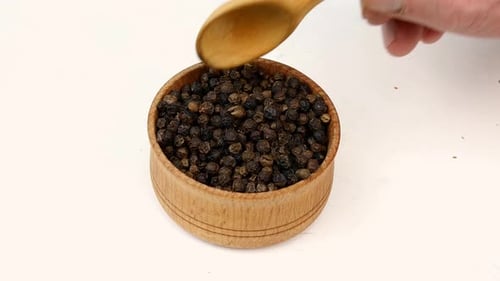 Scooping Black Peppercorns From Wooden Bowl