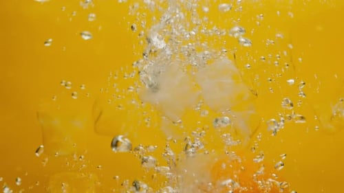 Oranges and Ice Cubes Falling in Refreshing Liquid
