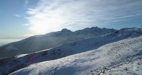 Forward Aerial Top View Over Winter Snowy Mountain with Ski Tracks in Sunny Day with Clouds