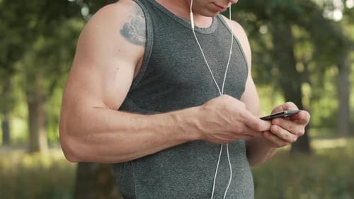 Man Using Smartphone with Earphones in Green Park