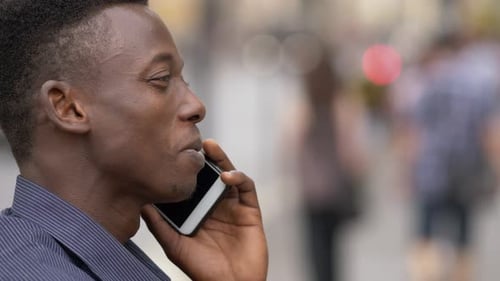 Smiling young american african man talking by phone in the street- profile