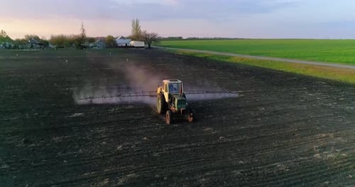 Tractor with trailed sprayer spraying chemicals on agricultural field. Aerial view.