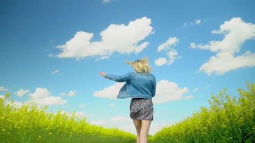 Woman Runs Quickly Through Meadow of Flowering Rapeseed Smiling Her Arms Open