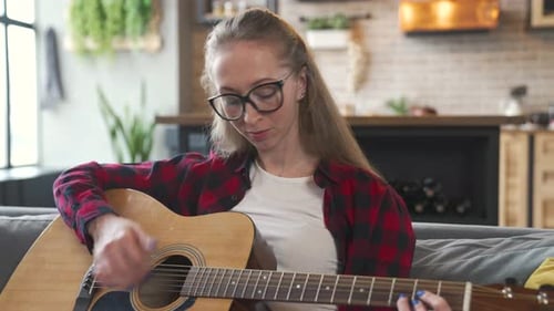 Young Adult Woman Playing Guitar on Couch at Home