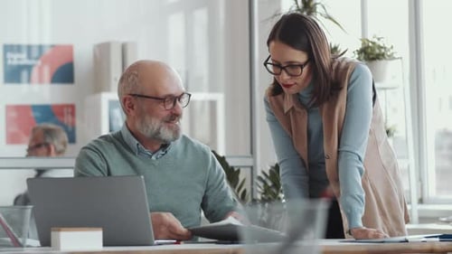 Senior Businessman Helping Young Female Colleague during Workday in Office