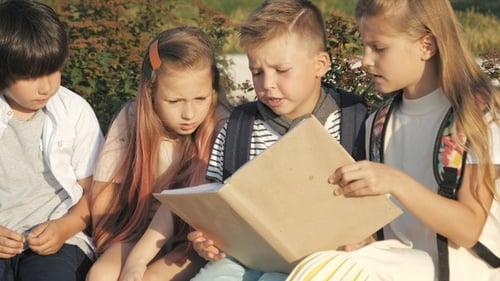 Pupils looking through encyclopaedia outdoors