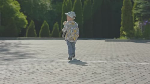 Lost Baby Boy Child in Cap Walking Street with Backpack and Teddy Bear in Hands