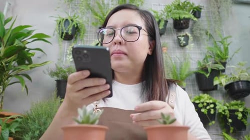 Front view of happy asian woman wearing glasses taking a picture of plants
