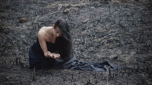 Woman Kneeling in Desolate, Charred Landscape