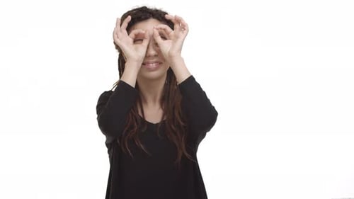 Junges und sorgloses Hipster-Mädchen mit Dreadlocks und Ohrtunneln, das Fingerbrillen oder Fernglas herstellt