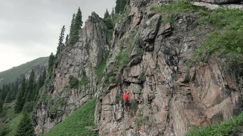 Man Athlette Climbing on the High Rock in the Mountains