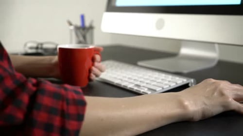 Person Working at Computer Holding a Mug