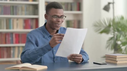 Young African Man Celebrating Success While Reading Documents in Office