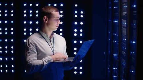 Man Working at Laptop in Data Center at Night