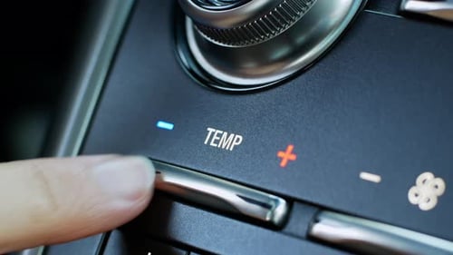 A woman lowers the temperature of the car's climate control by pushing a close-up chrome button