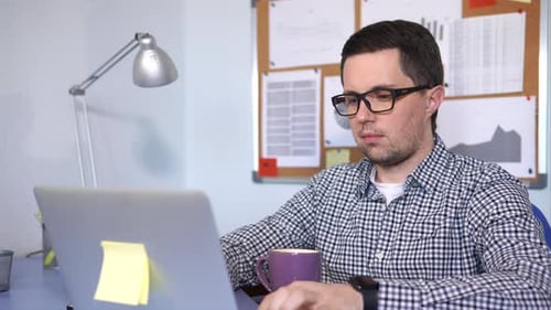 Man Drinking Coffee While Working on Laptop