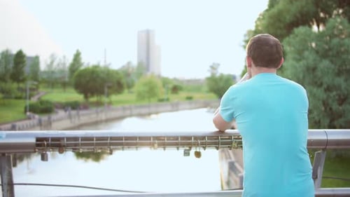Mann steht in einem Park auf einer Brücke und schaut auf den Fluss Kamerabewegung Rückansicht Kopierraum