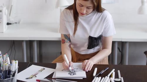 Fashion Designer Drawing Female Dress at Desk in Sewing Studio