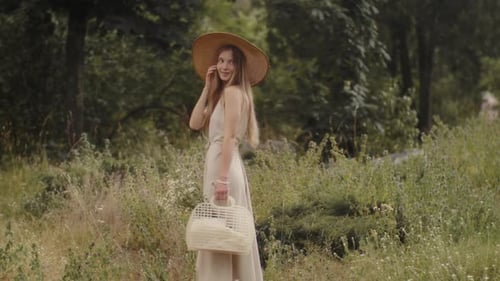 Woman in Dress and Straw Hat Strolls in Field