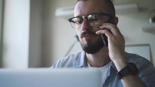 American Businessman Talking on Phone and Looking at Laptop Screen in White Office