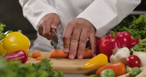 Chef slicing a carrot surrounded by fresh vegetables