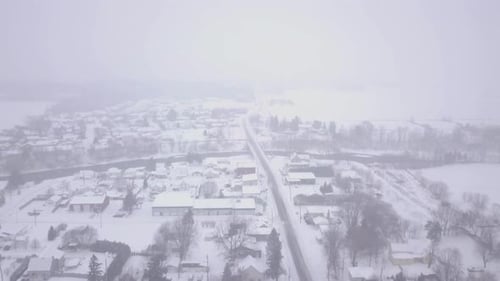 High aerial view flying backwards over a rural small town during a blizzard