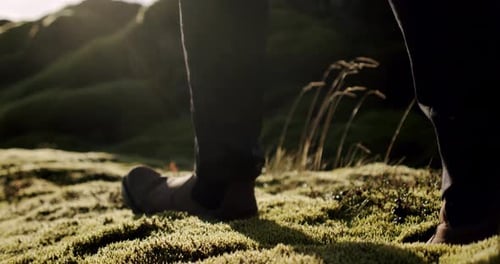 A Close Up View of a Man Legs in Brown Boots Walking on Green Moss and Grass in Iceland