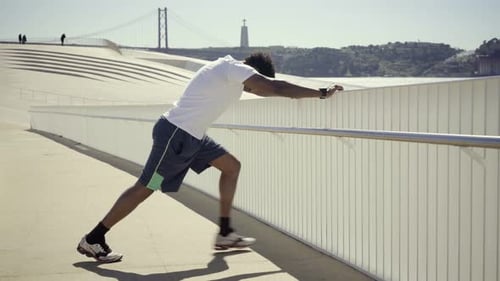 Young Adult Stretching Leg Muscles on Sunny Boardwalk
