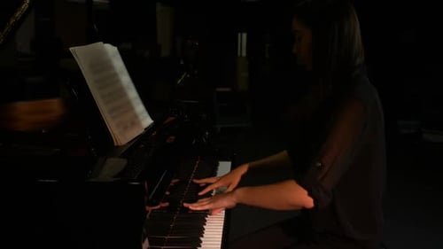 Woman plays a grand piano in a dark room