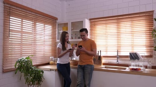 Young Couple Using Phones Together in Bright Kitchen