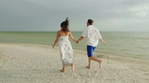 Young Man and Woman Hold Hands, Run Barefoot Along the Beach Happy Holidays and Honeymoon