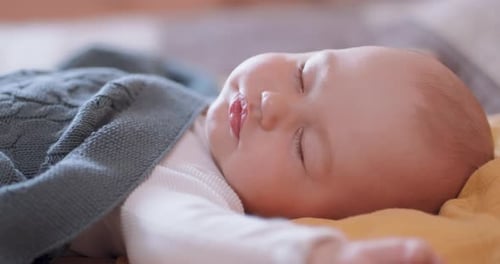 Close Up of Beautiful Sleeping Baby Under the Grey Blanket Who Turns Its Head Away From Camera