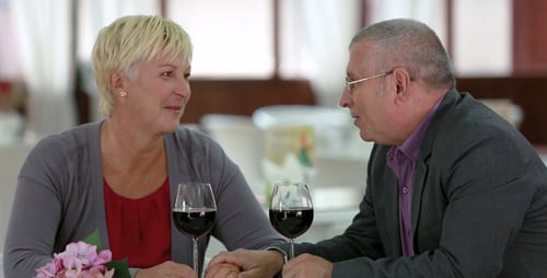 Mature Couple Holding Hands Over Wine at Restaurant