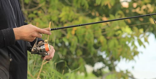 Person Fishing with Rod and Reel by River