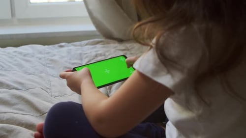 Kleines Mädchen benutzt ein Smartphone mit Greenscreen, während es zu Hause sitzt