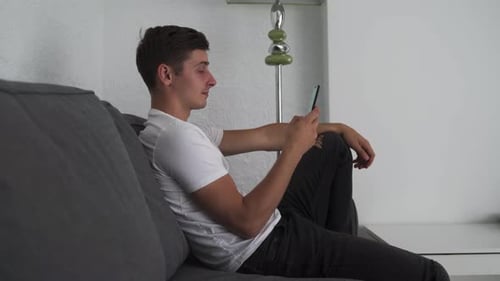 Young Adult Relaxing on Couch with Smartphone