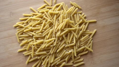 Uncooked Penne Pasta Pile on Wooden Surface