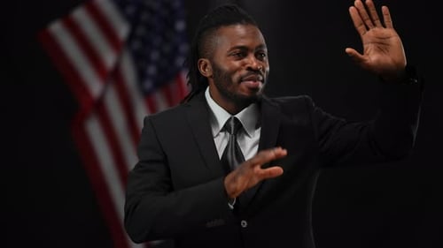 Portrait of Smiling African American Male Politician Greeting Public in Camera Flashes with USA Flag